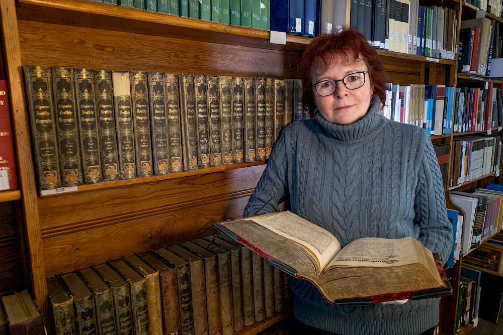 Karin Keller hält im Forschungssaal des Universitätsarchivs das 1632 angelegte Wittenberger Statutenbuch in der Hand, in das unter anderem ein Horoskop zum Gründungstag der Universität Wittenberg eingebunden ist.