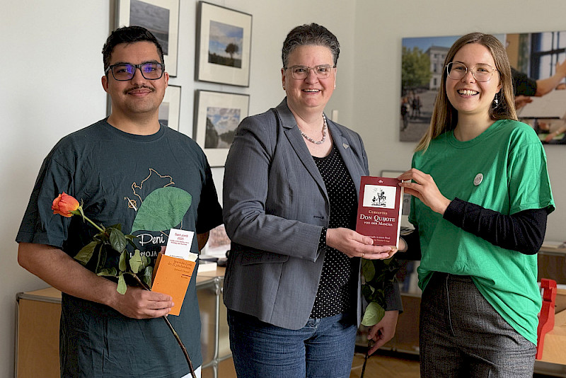 Die Studierenden Anna Demuth (rechts) und Maximilian Meyer schenkten Rektorin Claudia Becker eine Ausgabe des Don Quijote und eine Rose.