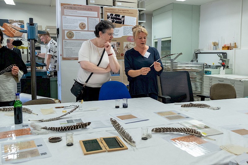 Mediävistin Simone Schultz-Balluff (rechts) erklärt der Rektorin die korrekte Handhabung einer Feder.